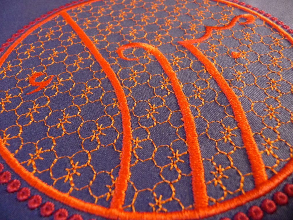 Stickerei arabische Schrift Mabruk, Glückwunsch, rot-orange auf violettem Hintergrund